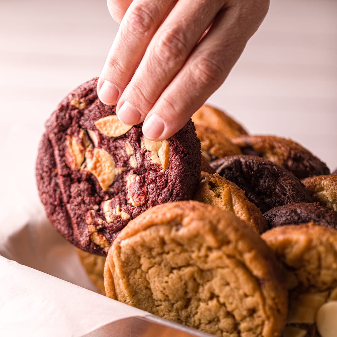 Mão pegando um cookie Red Velvet da bandeja da Monkey Cookie