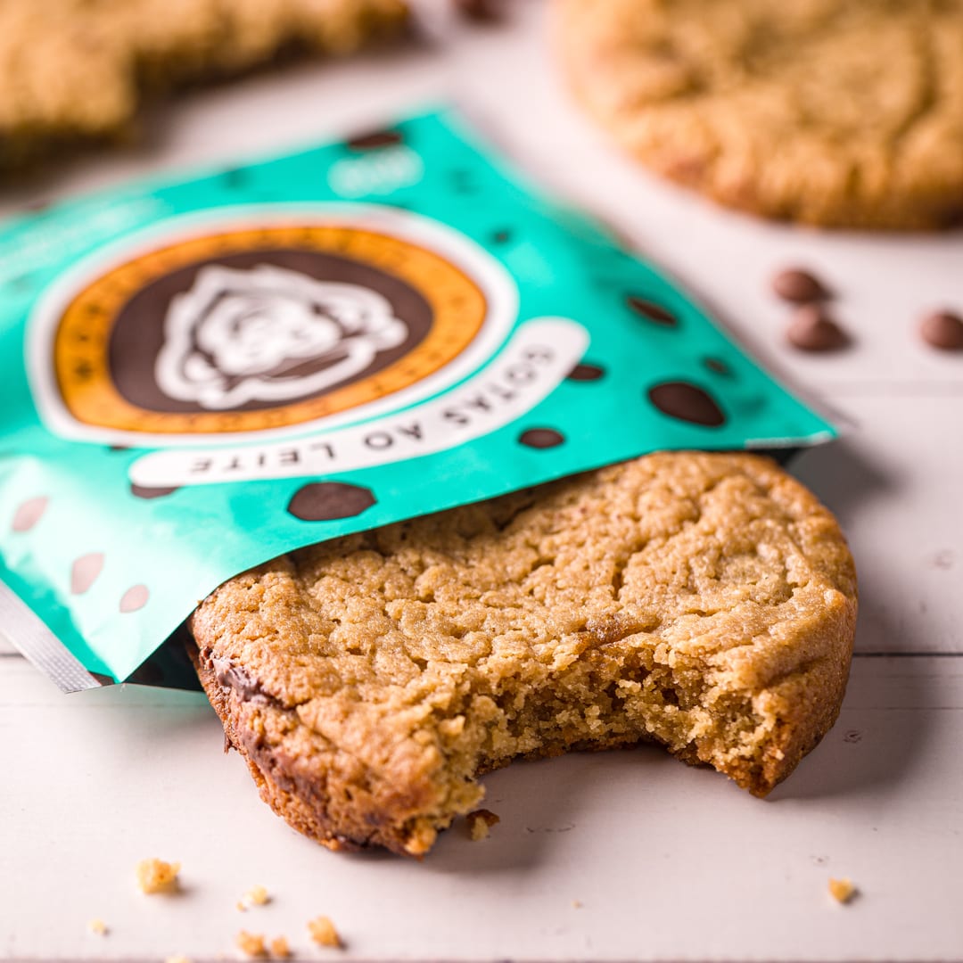 Cookie Gotas ao Leite mordido saindo da embalagem teal da Monkey Cookie